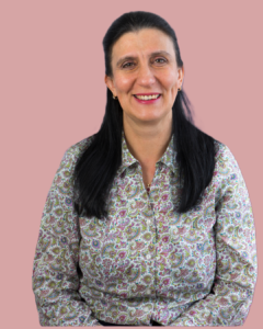 Woman with long dark hair wearing a patterned shirt, smiling against a pink background.